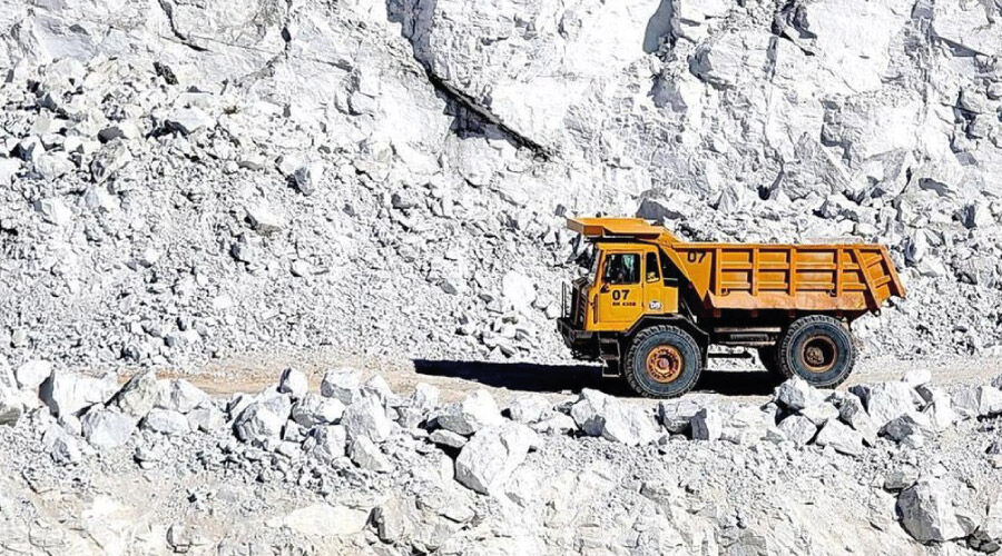 Trator amarelo transportando calcário em uma jazida.