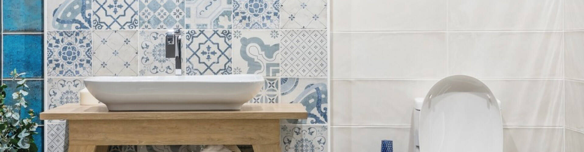   Banheiro com azulejos brancos e azuis, com espelho, pia retangular em cima de bancada de madeira, privada e itens de decora&ccedil;&atilde;o azuis e brancos.